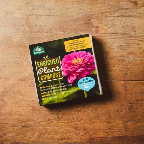 Enriched plant compost package with a pink flower on a wooden surface