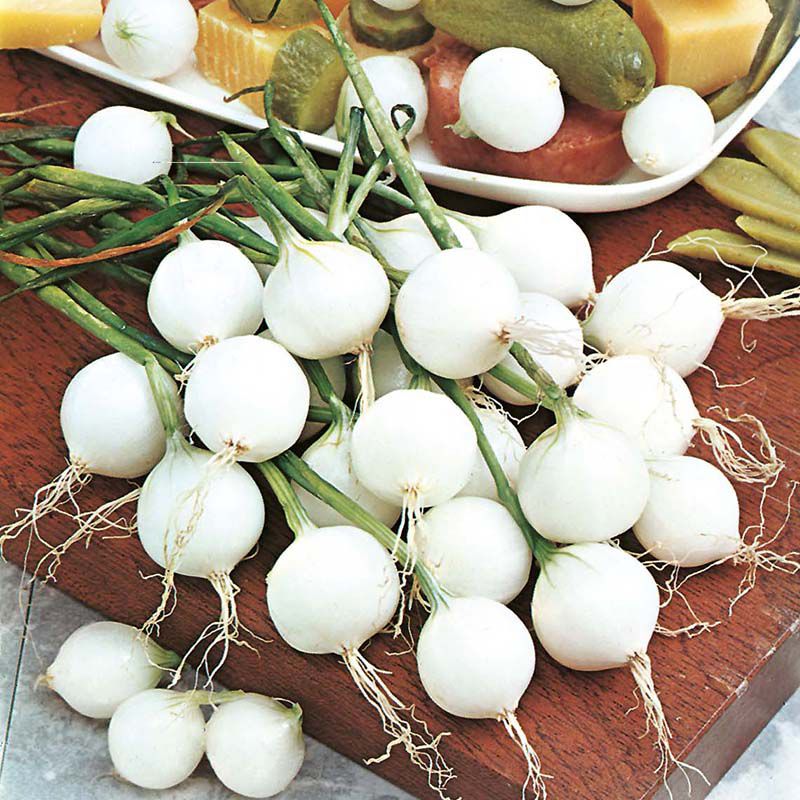 White onions on a wooden cutting board with a blurred background of vegetables.
