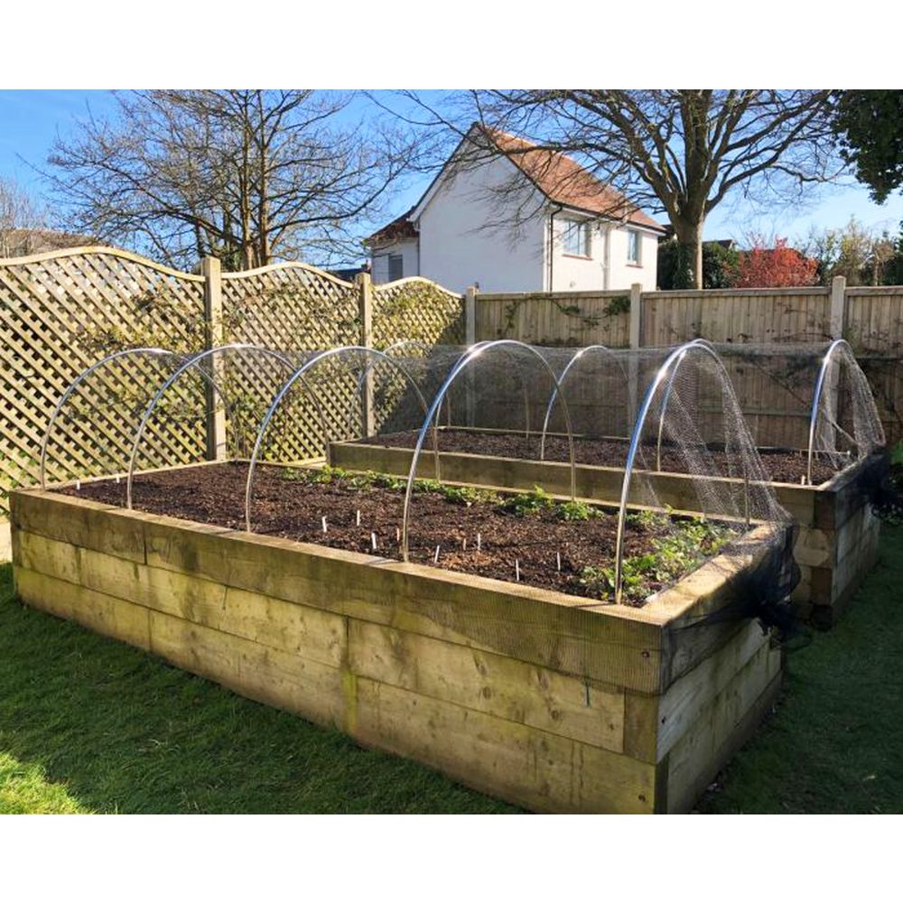 Wooden raised garden bed with clear plastic tunnel in a backyard setting.