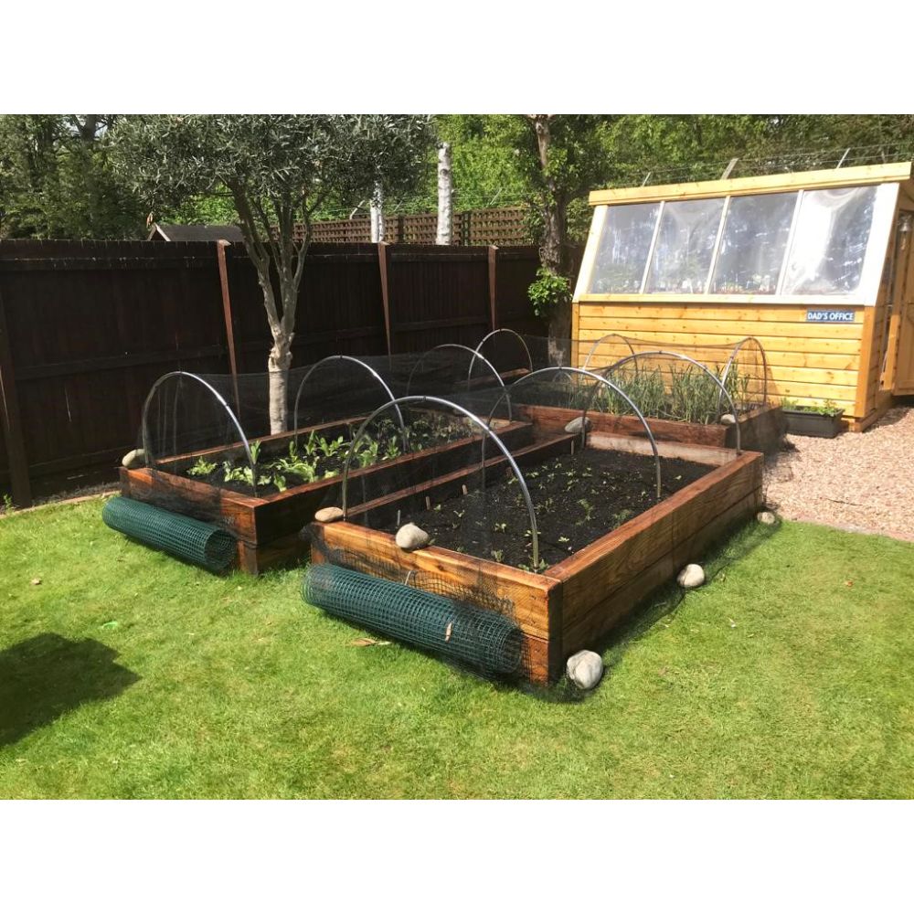 Wooden raised garden beds with trellises on a grassy area, with a greenhouse in the background.