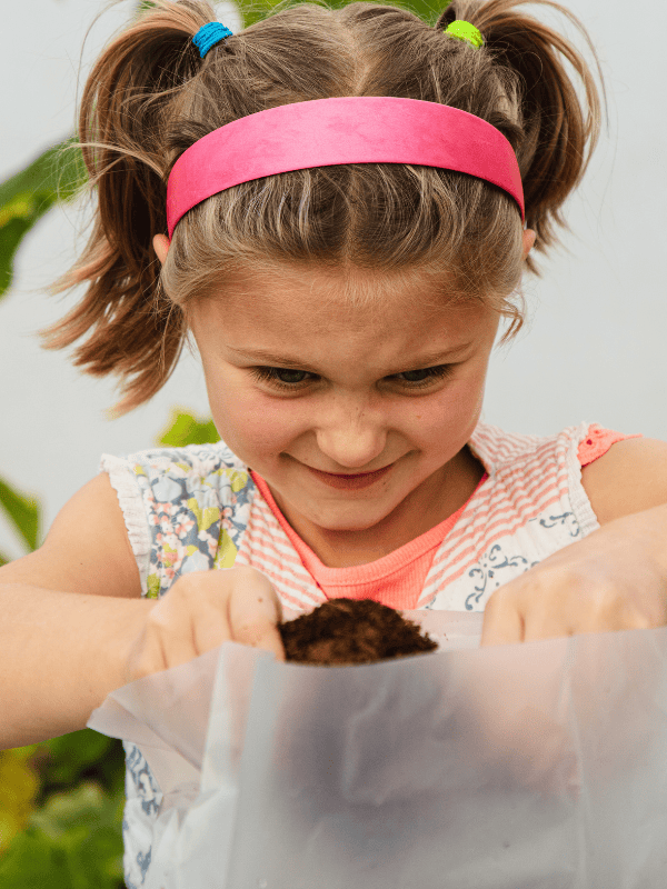 Young girl with pigtails and a pink headband holding a sample of soil.