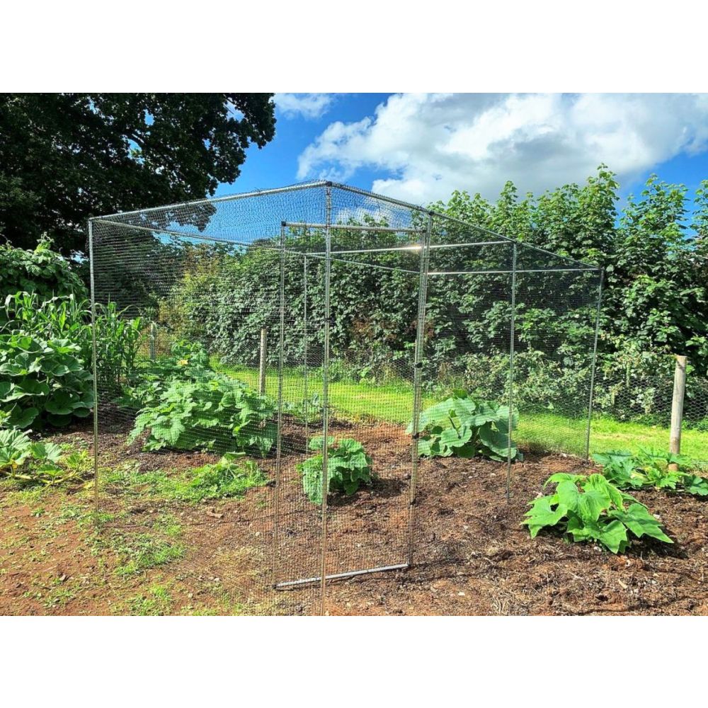 Metal chicken coop in a garden with plants and trees in the background